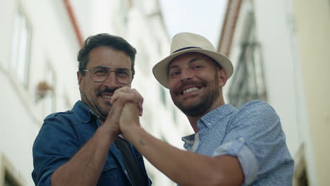 front view of gay couple looking at camera and joining hands