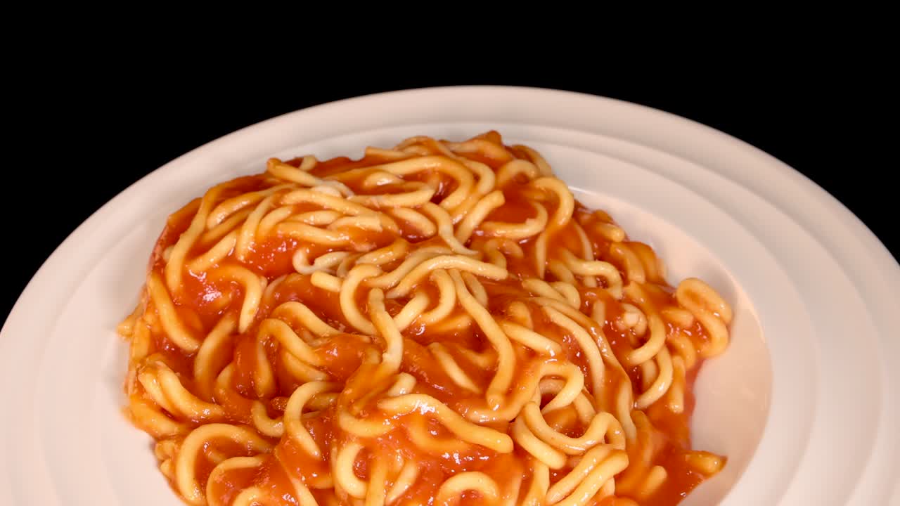 Cooked spaghetti in tomato sauce is dropped onto a clean white plate, captured in close-up with even studio lighting and a static camera angle