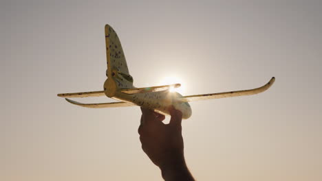 Hand-Mit-Einem-Spielzeugflugzeug-Auf-Einem-Hintergrund-Von-Himmel-Und-Sonne