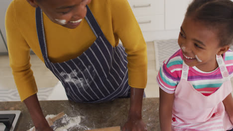 Happy-african-american-mother-and-daughter-wearing-aprons-having-fun-while-cooking-in-kitchen