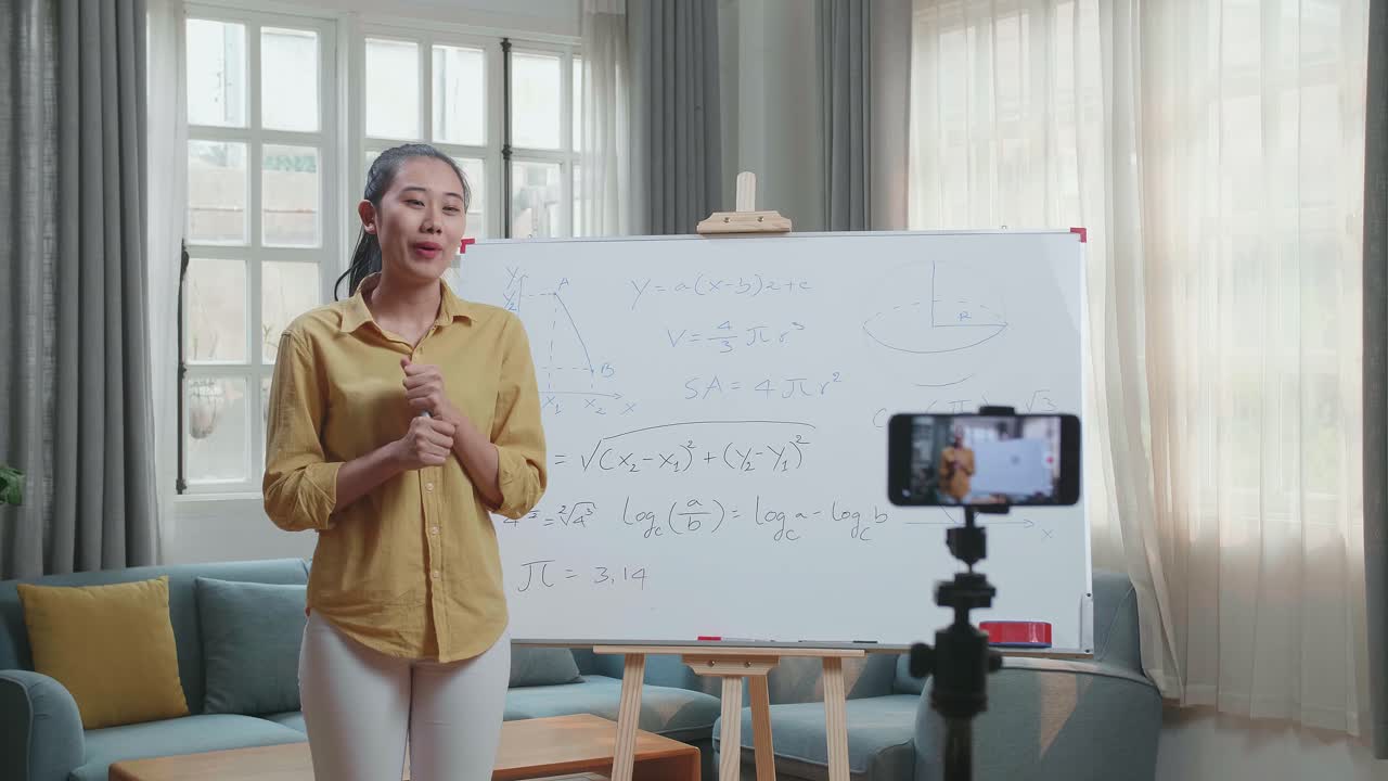 Azjatycka nauczycielka z markerem nagrywa wideo smartfonem, ucząc matematyki w domu.