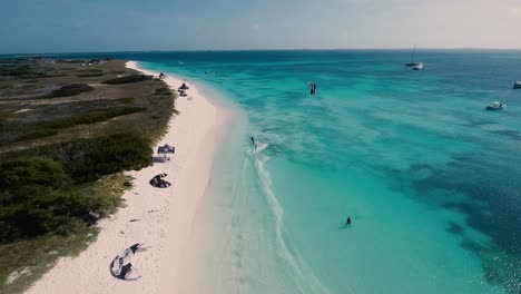 Man-kitesurfing-along-caribbean-white-sand-beach,-aerial-view-sunset-Los-Roques