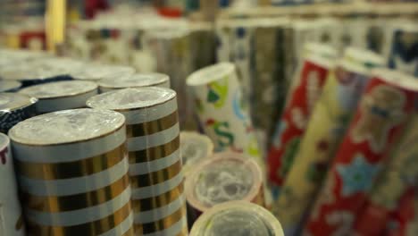 imágenes cercanas o de cerca de rollos de papel de envoltura coloridos y festivos en un supermercado a medida que las imágenes se mueven y se deslizan sobre ellos lentamente. los papeles de envoltura tienen diferentes diseños y colores festivos.