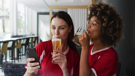 Diverse-group-of-happy-friends-watching-a-game-drinking-beers-and-taking-a-selfie-at-a-bar