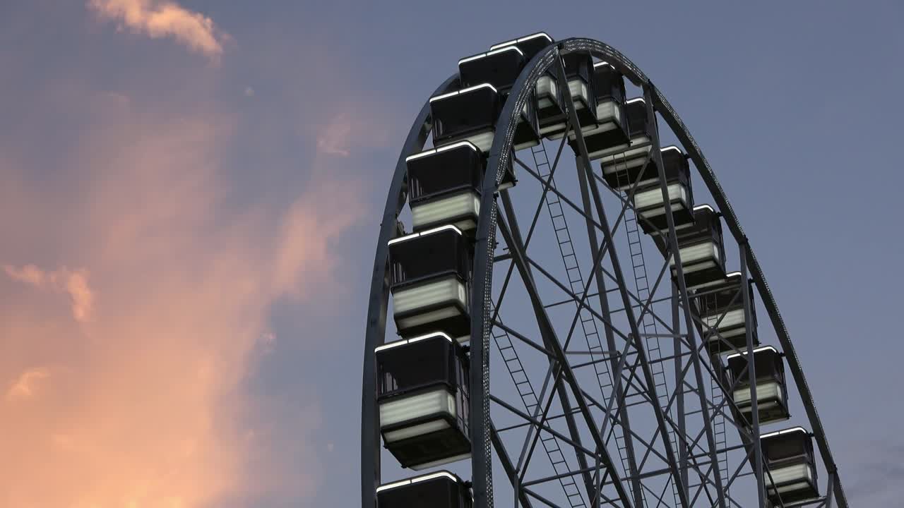 4K. Una ruota panoramica sta girando. È il tramonto. Nuvole arancioni.