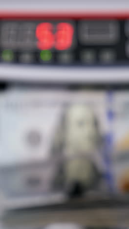 automatic machine counting dollar banknotes. modern banking activity. blurred background. hand is taking a pack of counted dollar bills from the counter machine. vertical video