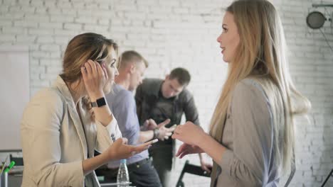 office employee communicate with each other. two businesswomen are talking with each other in office and using a smartphone. female is searching something on her mobile phone