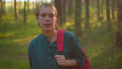 exhausted hiker walking through peaceful forest, adjusting red bag strap on shoulder, gazing thoughtfully around, bathed in warm sunlight that casts a gentle glow on her face