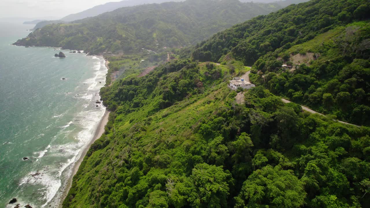 A white house on a hill overlooking a tropical beach and lush greenery, aerial view