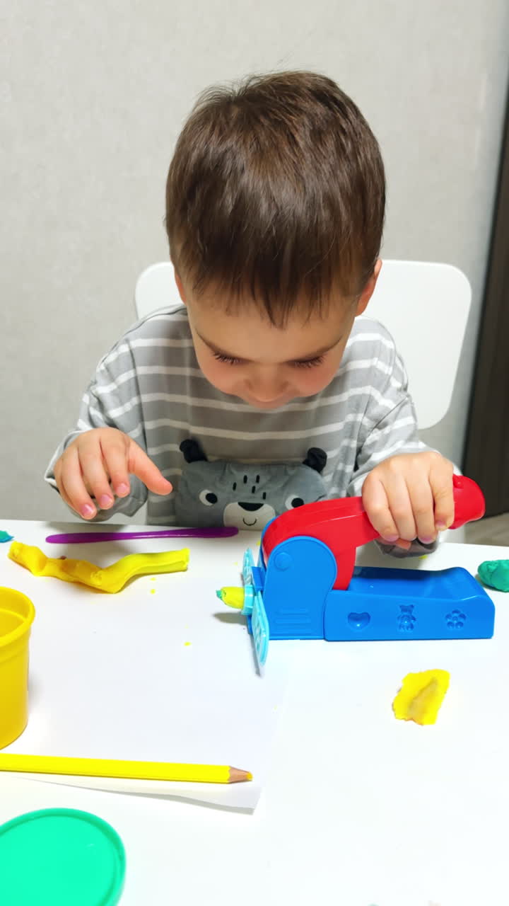 Concentrated Caucasian baby places some plasticine into the molding device. Cute kid smiles into camera and presses the lever of a machine. Vertical video.