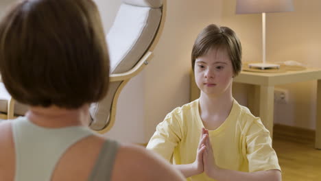 niña con síndrome de down imitando a su madre haciendo postura de yoga en casa