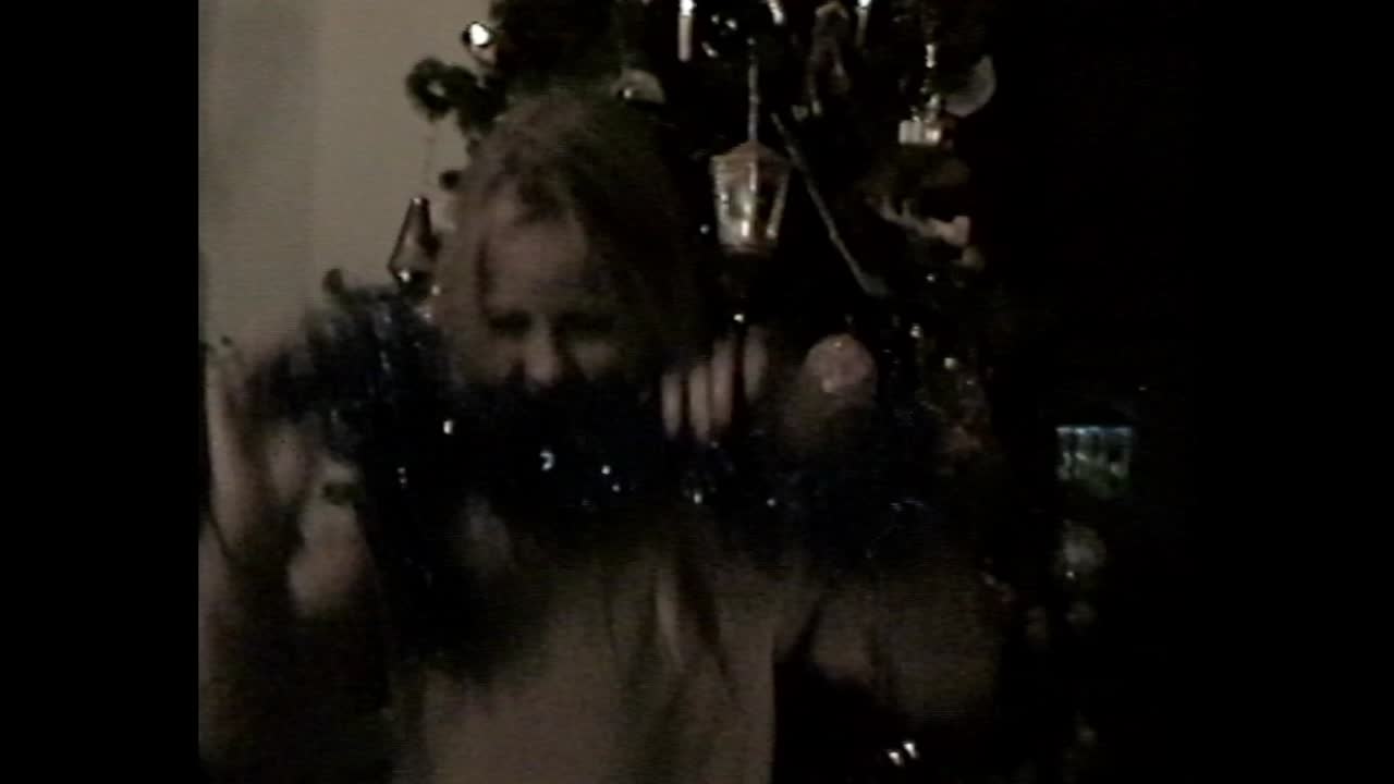 Child standing by Christmas tree with tinsel scarf
