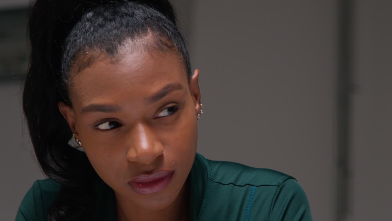 체육관에서 운동 훈련을 하고, 옷차림실에서 앉아서 집중하고, 집중된 표정으로 운동을 하는 여성 선수의 근접한 초상화.