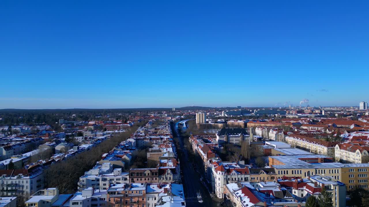 Paesaggio urbano di Berlino ripreso dall'alto, che mostra tetti innevati, edifici cittadini e strade sotto un cielo azzurro brillante. Fantastica veduta aerea con drone in ascesa.