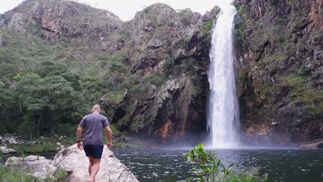 male tourist walks to edge of pool below fundao waterfall in brazil