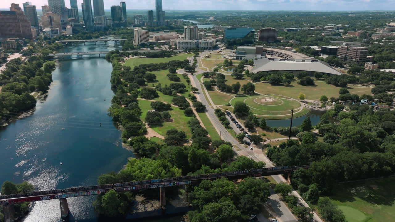 Cinematic drone orbit around Auditorium Shores and Ladybird Lake reveals the Austin, Texas skyline under soft morning light. Calm atmosphere, glassy water, and urban greenery, aerial view