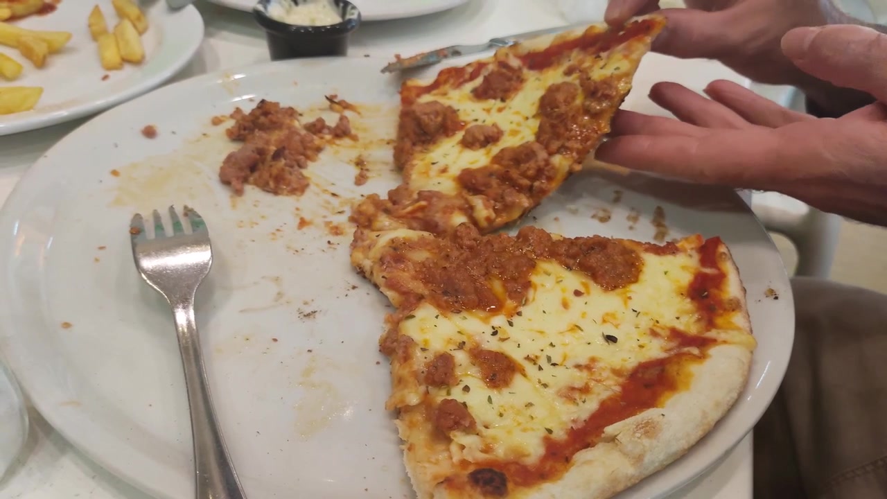 Primo piano di mani che prendono e spezzano una fetta di pizza barbecue al ristorante.