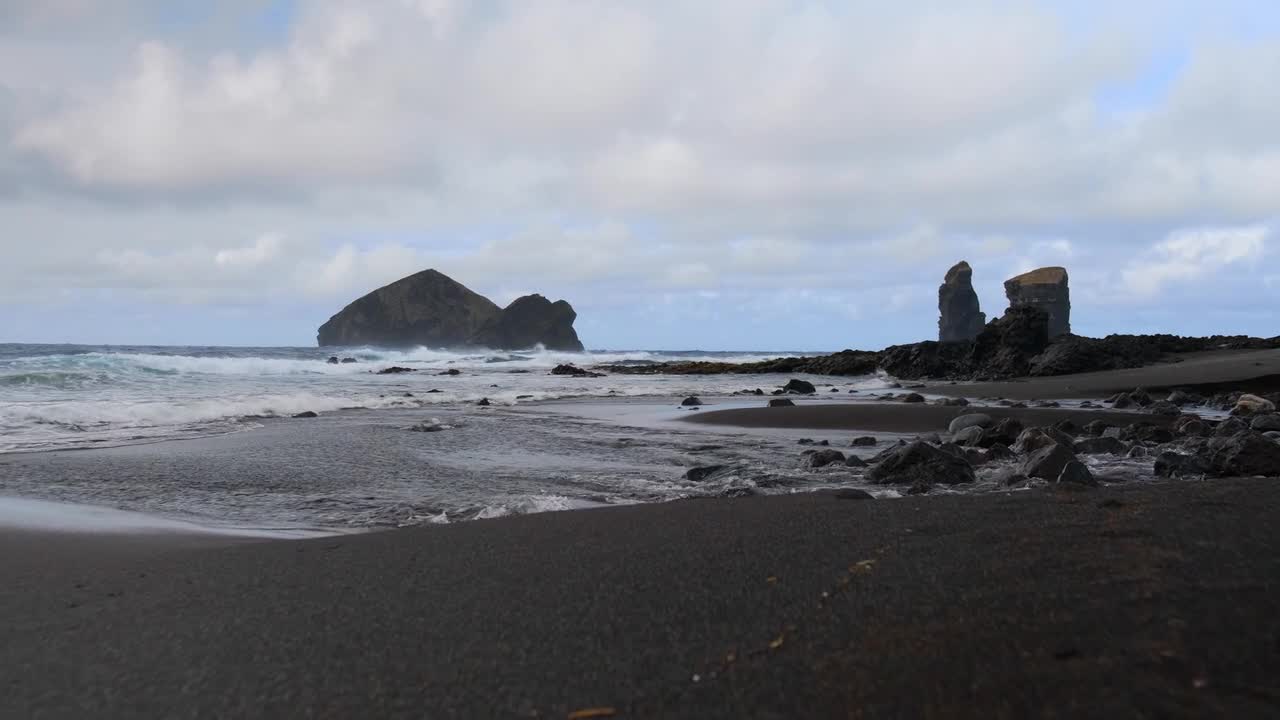 Dramatic black sand beach at Reynisfjara, Iceland, with striking basalt sea stacks under a moody sky. Volcanic shoreline, cinematic atmosphere, and textured terrain add to the allure