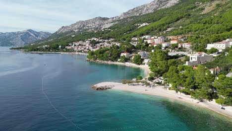 Dron-Panorámico-Lento-Aéreo-Playa-Brela-Croacia-Mar-Azul-Playa-Bordeada-De-Pinos