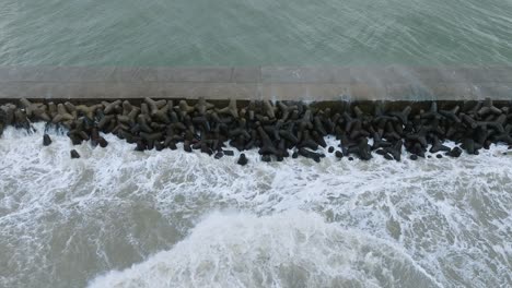 Vista-Aérea-Del-Muelle-De-Concreto-Del-Puerto-De-Liepaja,-Tormenta-De-Otoño,-Grandes-Olas-Salpicando,-Día-Nublado,-Amplio-Disparo-De-Drones-A-Vista-De-Pájaro