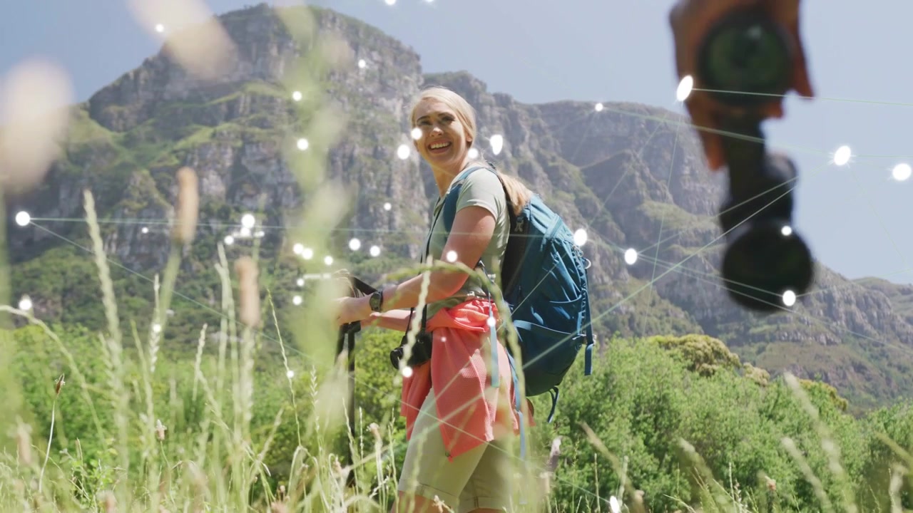 Woman hiking waving in meadow lights overlaying bags as partner approaching turning walking to peak