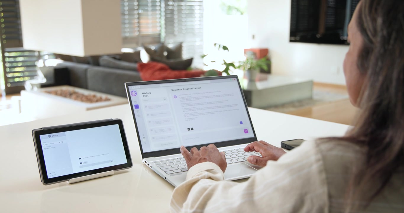 African American woman editing proposal on laptop, replying to tablet chat at counter, copy space