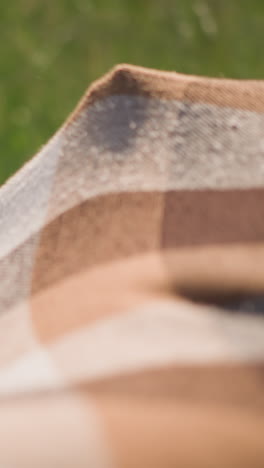a little boy in a white shirt walks into a flowing plaid scarf in a sunny grassy field. another child, whose face is not visible, holds the scarf as the boy smiles with joy