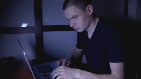 joven trabajando y escribiendo en su laptop en la oscuridad