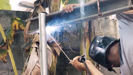 professional welder employing industrial welding machine to put together two pieces of metal creating a metalic structure as part of his daily work at a local small business