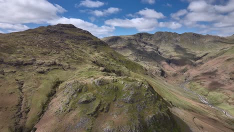 flying towards green and craggy mountain buttress with blue sky cloud shadows moving across the crinkle crags range behind