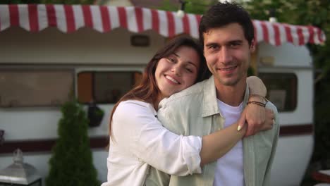 retrato de una pareja romántica hombre y mujer sonriendo mientras se abrazan cerca de la casa sobre ruedas al aire libre. remolque de estilo retro en el fondo