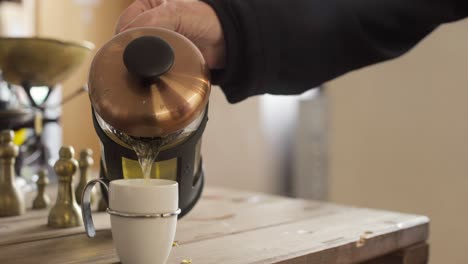 Glass-French-press-tea-maker-used-to-pour-brewed-green-tea-into-a-white-cup-placed-on-the-table-with-chess-game