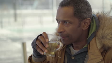 Pensive-middle-aged-man-drinking-hot-beverage-in-cafe