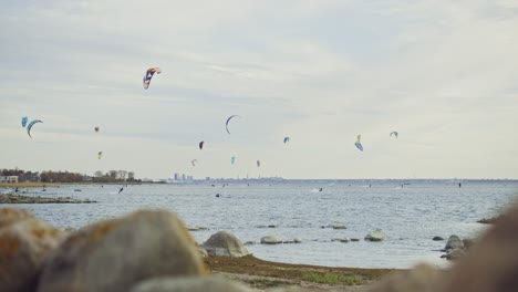 Skilled-kite-surfers-in-slow-motion-gliding-across-the-picturesque-Nordic-coastline-of-Estonia,-framed-by-the-iconic-silhouette-of-the-capital-city,-Tallinn