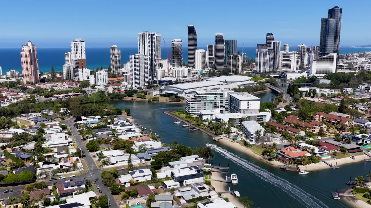 Drone camera glides above river, luxury homes, and high-rise skyline under bright daylight