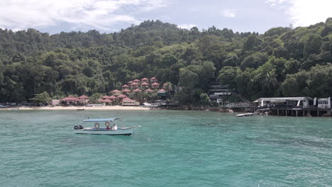 aerial video of a boat floating on anchor in front of a remote island resort. filmed at the alunan resort, perhentian kecil, malaysia. slow dolly forward above the ocean.