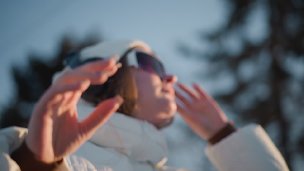Side view of student adjusting tinted sunglasses under clear sky wearing white beanie and puffer coat breeze tousles hair sunshine reflects off visor conveying cheerful winter fashion mood