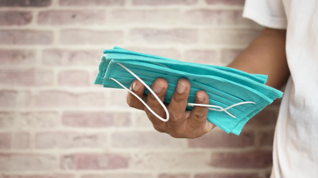 persona que sostiene una pila de máscaras faciales de color azul claro