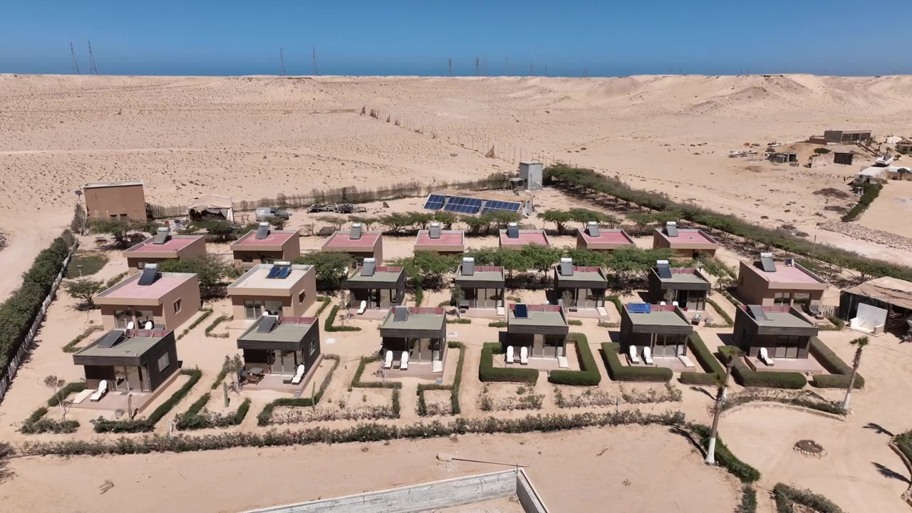 Drone-ilmakuva luksushuviloista ja maisemoiduista puutarhoista autiomaan lomakohteessa lähellä Dakhlaa, Marokossa. Moderni majoituspalvelujen kehityshanke Marokon Saharan laajoissa maisemissa.