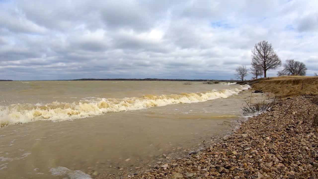 Strong winds after winter storm causes muddy ocean like waves to crash on a small beach on a Texas lake near a public marina