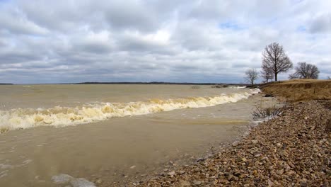 strong winds after winter storm causes muddy ocean like waves to crash on a small beach on a texas lake near a public marina