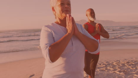 african american senior couple practicing yoga together at the beach