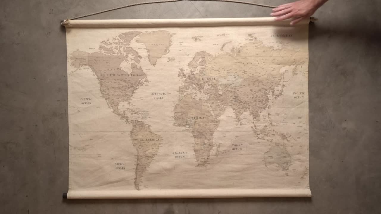 las manos de un hombre desenrollan un gran mapa del mundo sobre un fondo gris y concreto