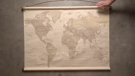 a man's hands unroll a large world map on a grey, concrete background