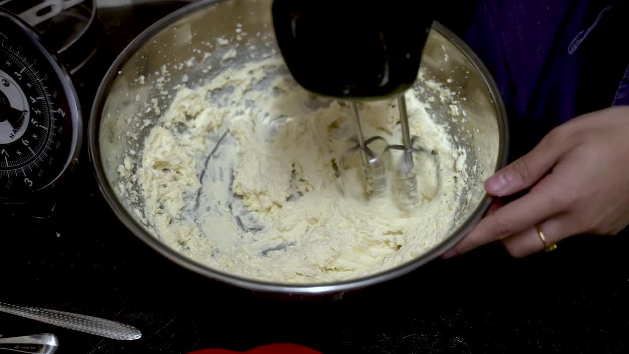 Close up of a pastry chef whisking flour and butter in a bowl with an electric mixer, preparing ingredients for a cake