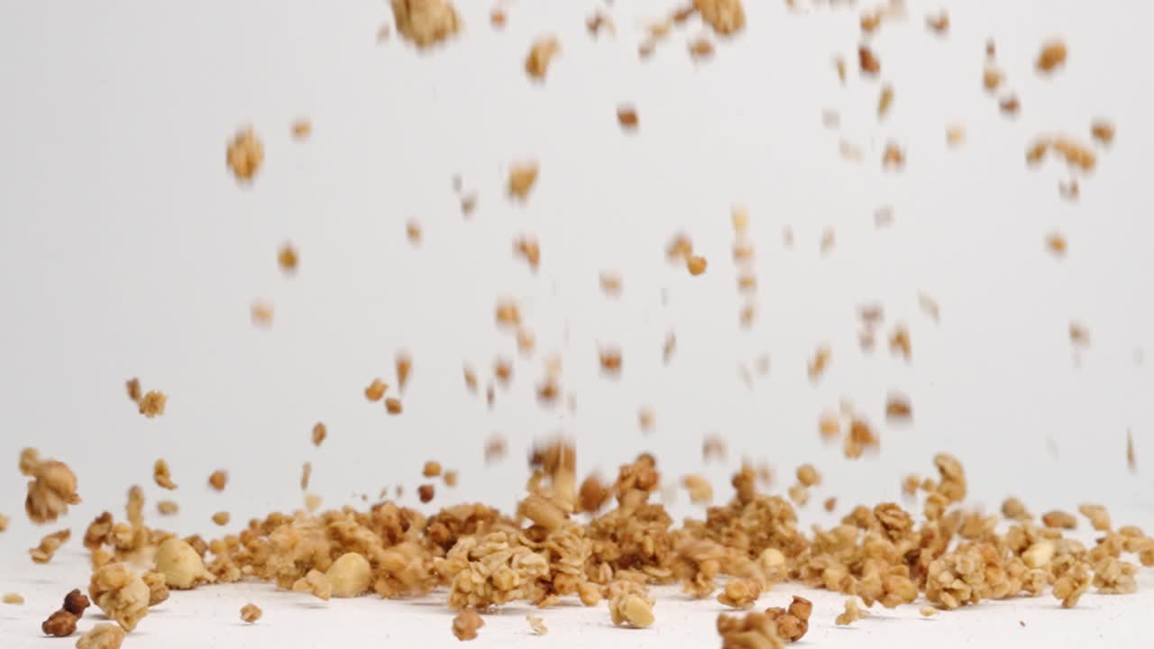 granola crujiente, avena y nueces cayendo sobre la mesa blanca en un montón a cámara lenta