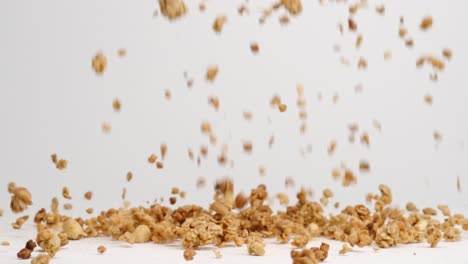 crunchy granola, oats and nuts falling onto white table top into pile in slow motion