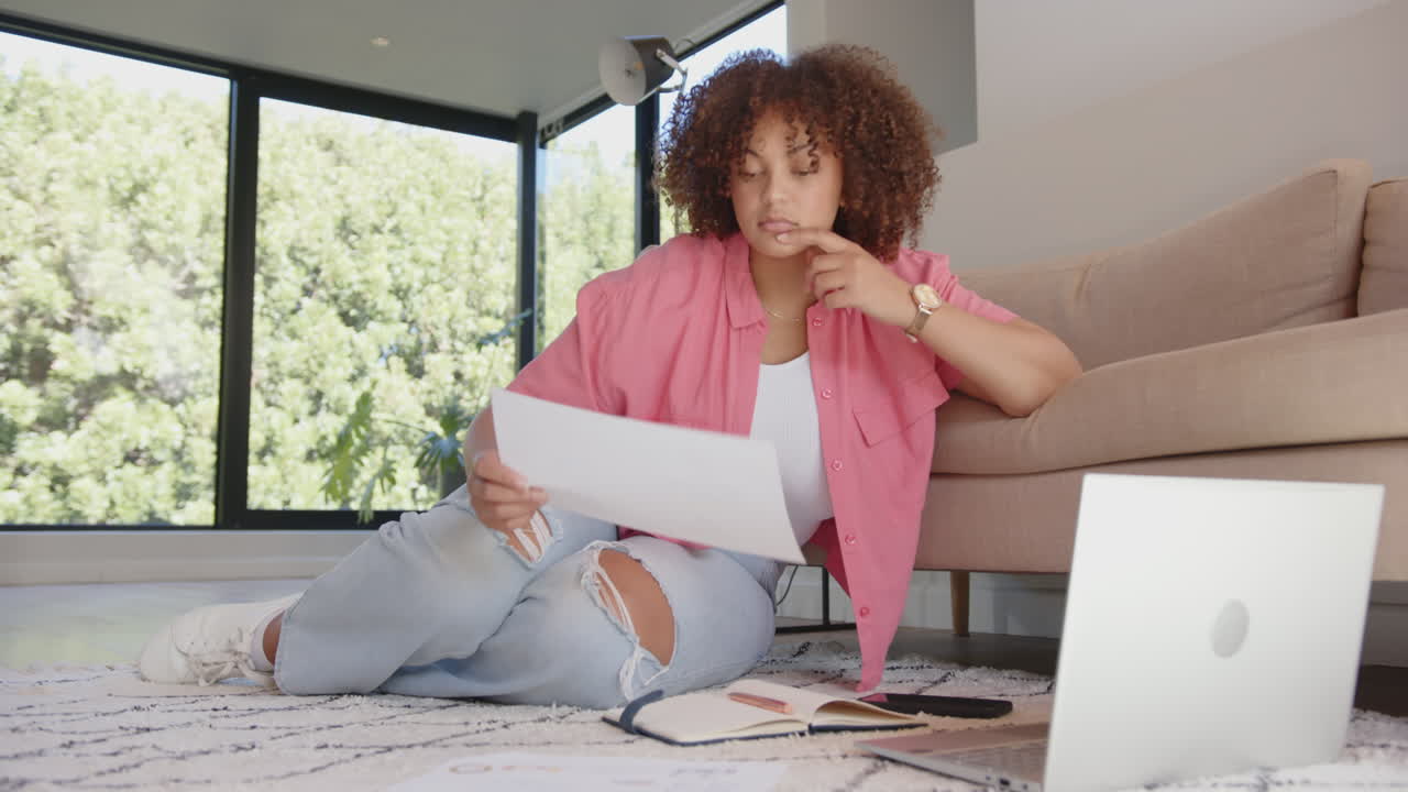 Reviewing documents, woman sitting on floor with laptop and notebook nearby