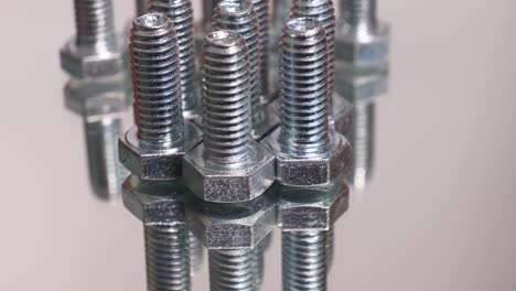 rotating group of galvanized metallic screws close-up. stainless steel bolts isolated on mirror reflective background.