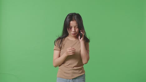 young asian woman victim of violence with bruise on face crying and talking on smartphone asking for help on green screen background in the studio